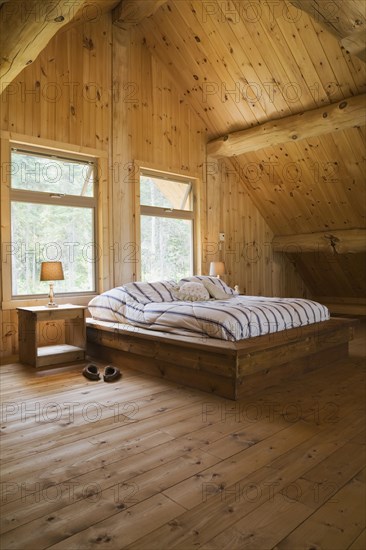 King size bed with wooden frame in master bedroom on upstairs floor inside handcrafted Eastern white pine Scandinavian log cabin home, Quebec, Canada, North America