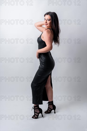 Vertical studio photo with grey background of a sensual woman with long night dress posing looking at camera