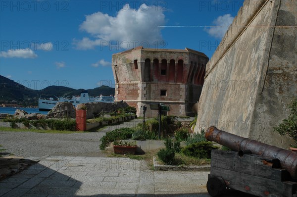 Old fortress with cannon in the foreground and a ship on the sea in the background Elba Island Italy