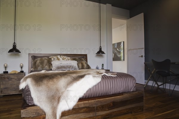 Queen size wooden base bed covered with fur pelt throw in guest bedroom inside luxurious home, Quebec, Canada, North America