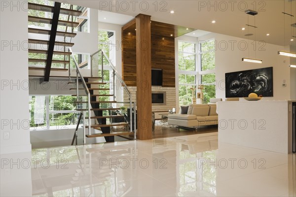 Wood, metal and glass staircase leading to living room with creamy beige L-shaped leather sofa inside luxurious home, Quebec, Canada, North America