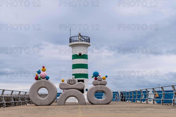 A playful striped lighthouse adorned with balloons on a pier beside the ocean, in Ulsan, South Korea, Asia