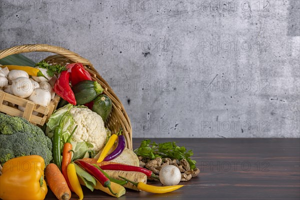 Various fresh vegetables such as peppers, cauliflower, peppers, mushrooms and broccoli in a basket on a wooden surface