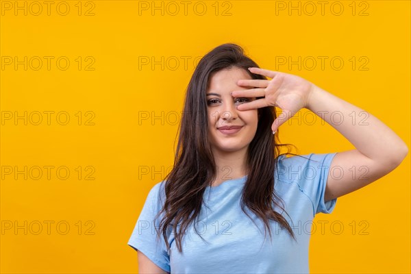 Studio portrait with yellow background of a caucasian woman hiding on the palm of the hand smiling
