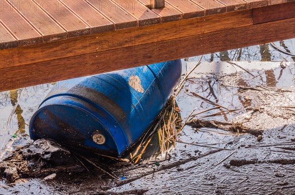 A raised deck beside a creek with a blue barrel partially hidden underneath, in South Korea