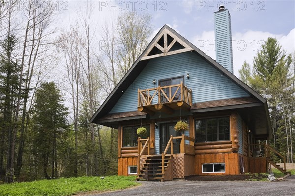 Post and beam cottage style hybrid log home facade with blue clapboard trim and timber elements in spring, Quebec, Canada, North America