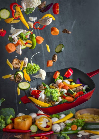 Colourful vegetables are thrown up from a pan while cooking, dark background