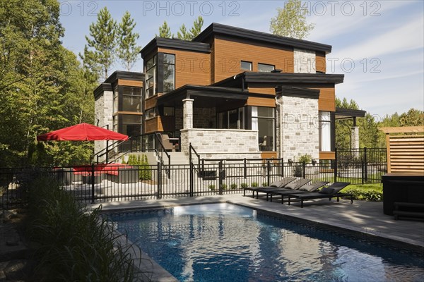 Two story grey, beige and tan cut stone with wood siding and black trim home and inground swimming pool in summer, Quebec, Canada, North America