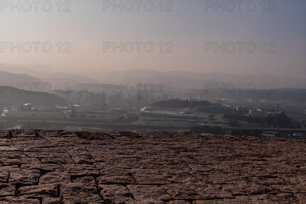 Top of mountain fortress wall made of flat stones with rural community under hazy sky in background in Boeun, South Korea, Asia