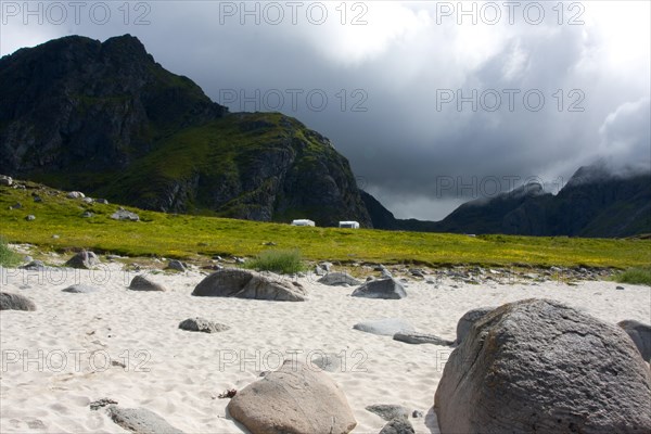 View of a dramatic mountain landscape with meadow, stones and a cloudy sky Lofoten