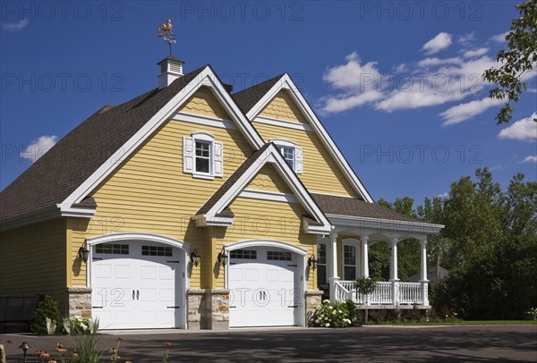 Yellow and white trim contemporary country house with two car garage, landscaped front yard and black asphalt driveway in summer, Quebec, Canada, North America