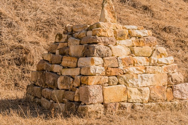 Closeup of pyramid shaped rock structure in field of brown grass at foot of hillside in Boeun, South Korea, Asia