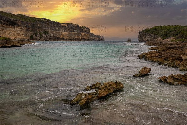 Rocky coast, long bay by the sea at sunset. Dangerous view of the Caribbean Sea. Tropical climate at sunset in La Porte d'Enfer, Grande Terre, Guadeloupe, French Antilles, North America