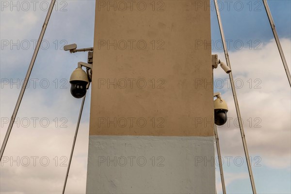 Two closed circuit cameras mounted on concrete bridge column with cloudy sky in background in South Korea