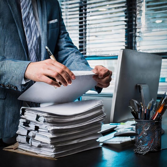 An entrepreneur organises documents at his desk with his laptop open and under time pressure, symbolism bureaucracy, AI generated, AI generated