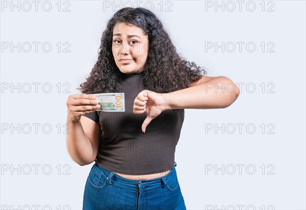Displeased young woman holding a dollar bill with thumb down isolated. Sad girl holding a a 100 dollar bill with thumb down