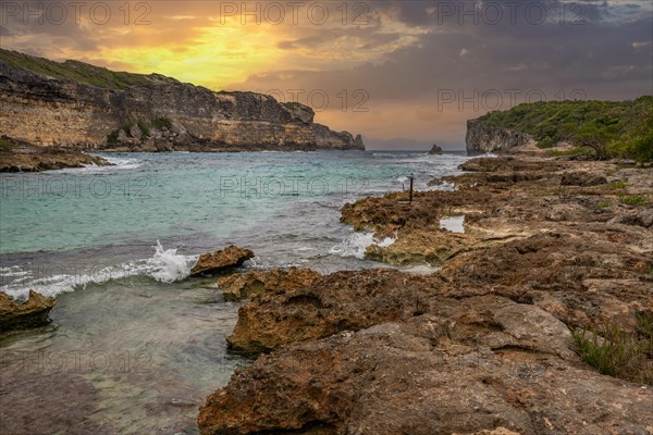 Rocky coast, long bay by the sea at sunset. Dangerous view of the Caribbean Sea. Tropical climate at sunset in La Porte d'Enfer, Grande Terre, Guadeloupe, French Antilles, North America