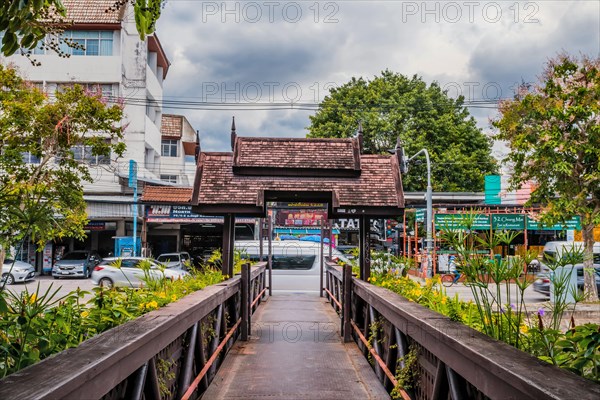 Traditional wooden bridge over a canal, with lush foliage and a city backdrop, in Chiang Mai, Thailand, Asia