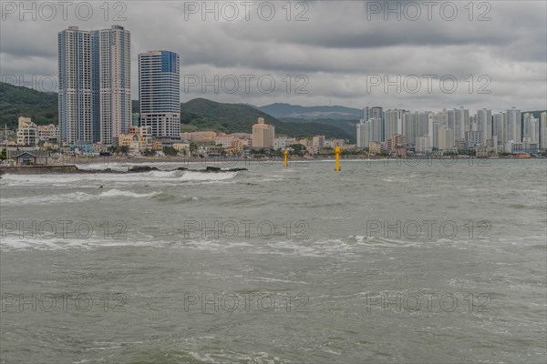 Overcast view of a city coastline with choppy sea, skyscrapers, and distant hills, in Ulsan, South Korea, Asia