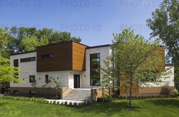 Beige stone with brown stained cedar wood modern cubist style residential home facade in spring, Quebec, Canada, North America