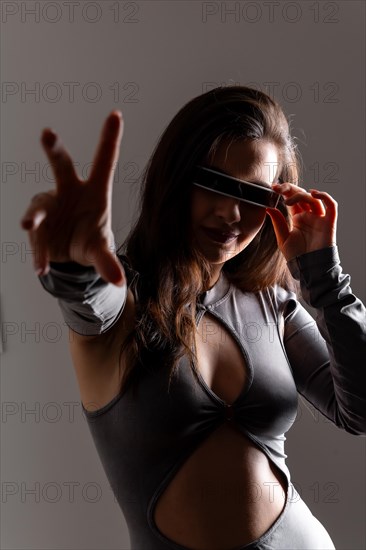 Studio portrait with grey background of a woman gesturing using futuristic artificial intelligence goggles