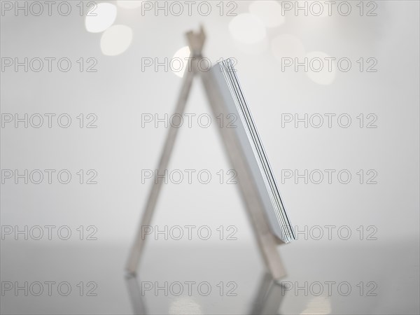 Mini easel in white made of wood, standing on a reflective smooth surface, white background with small lights, Germany, Europe