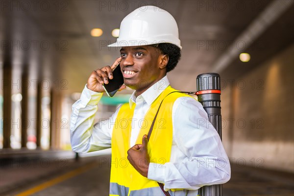 Side view close-up portrait of a busy young african architect wearing protective gear talking to the mobile in the city