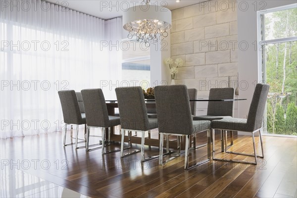 Glass dining table with gray upholstered high back chairs in dining room inside luxurious home, Quebec, Canada, North America