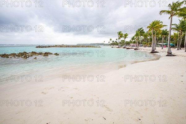 Caribbean dream beach with palm trees, white sandy beach and turquoise-coloured, crystal-clear water in the sea. Shallow bay on a cloudy day. Plage de Sainte Anne, Grande Terre, Guadeloupe, French Antilles, North America