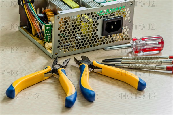 Side view of opened desktop power supply together with pliers and screwdrivers needed to repair device