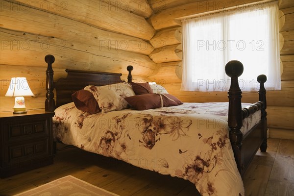 Antique four poster queen size bed with floral motifs bedspread in guest bedroom inside handcrafted Eastern white pine Scandinavian log cabin home, Quebec, Canada, North America