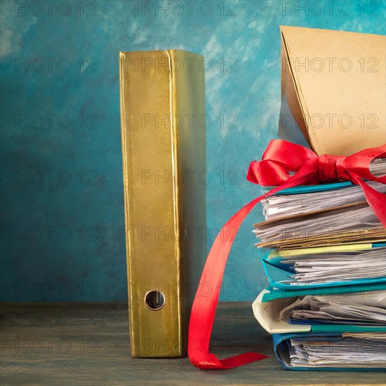 A golden folder next to a pile of papers, both wrapped with a red ribbon, symbolising bureaucracy, AI generated, AI generated