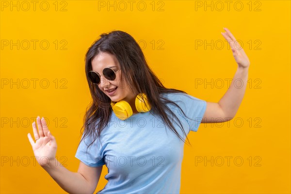 Studio portrait with yellow background of a woman with sunglasses dancing with headphones on lying on the neck