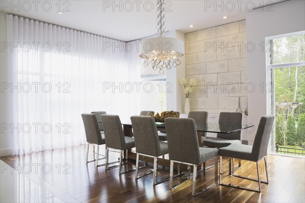 Glass dining table with gray upholstered high back chairs in dining room inside luxurious home, Quebec, Canada, North America