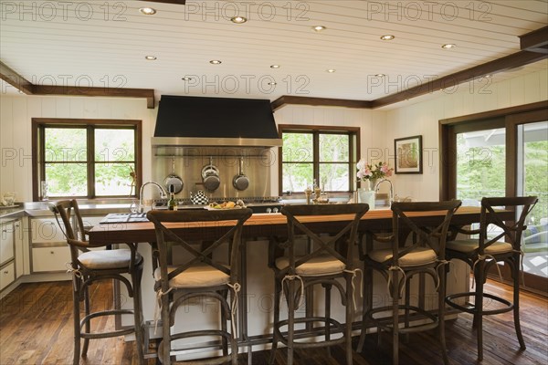 Country style kitchen with island and rustic wooden high chairs inside New Hampton style home, Quebec, Canada. This image is property released