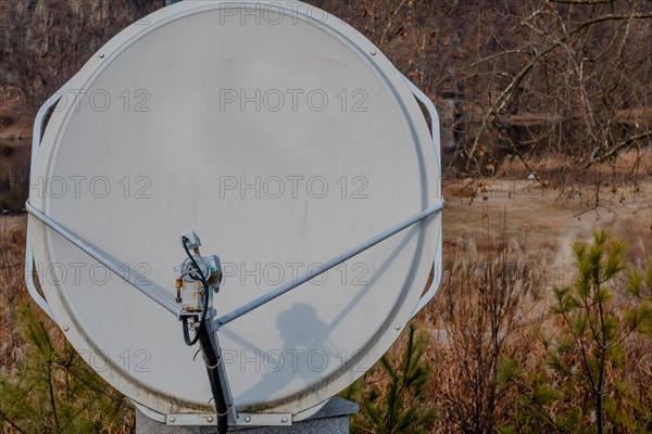 Closeup of satellite dish mounted on concrete column with riverside slightly blurred in background in South Korea