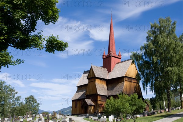 A traditional Norwegian stave church with a red roof under a clear blue sky surrounded by a cemetery Ringebu Lofote Stave Church