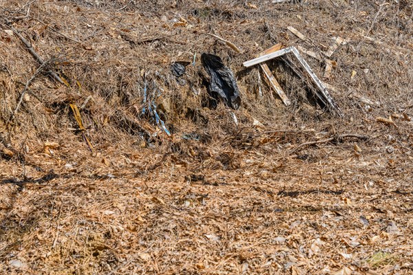 Discarded trash and black plastic bags pollute a dry grassy area, in South Korea