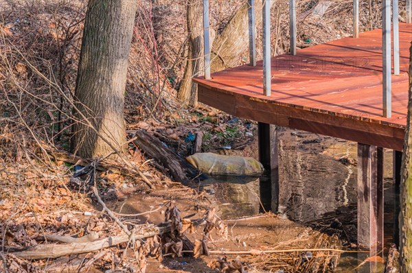 A raised deck beside a creek with a blue barrel partially hidden underneath, in South Korea