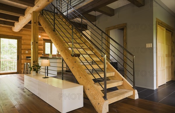 Wooden log stairs with black wrought iron railings and long cabinet table inside contemporary style log home, Quebec, Canada, North America