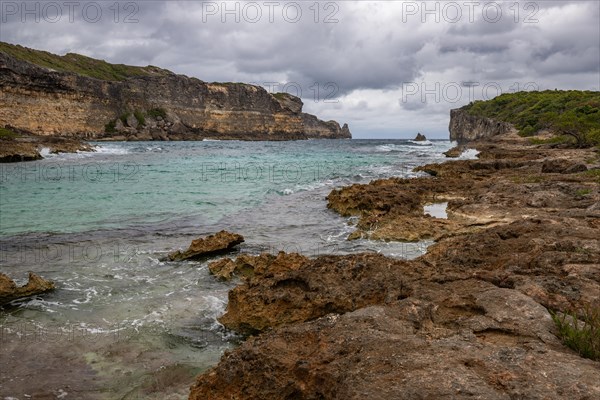 Rocky coast, long bay by the sea at sunset. Dangerous view of the Caribbean Sea. Tropical climate on a cloudy day in La Porte d'Enfer, Grande Terre, Guadeloupe, French Antilles, North America