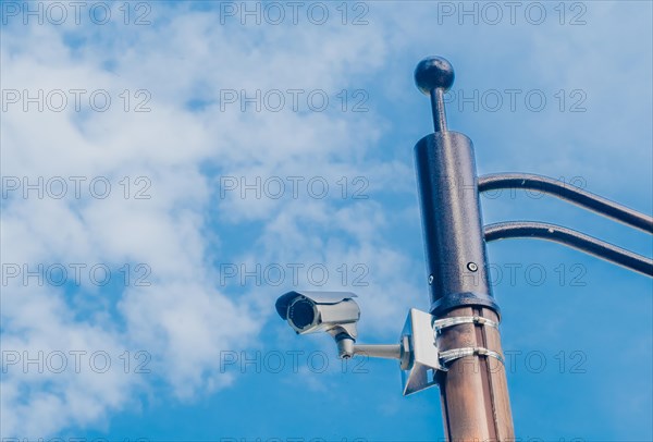 Surveillance camera mounted on metal light pole with blue sky and puffy white clouds in background in South Korea