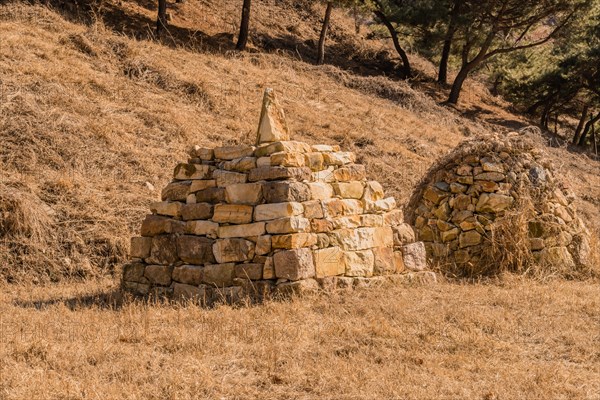 Two pyramid shaped rock structures in field of brown grass at foot of hillside in Boeun, South Korea, Asia