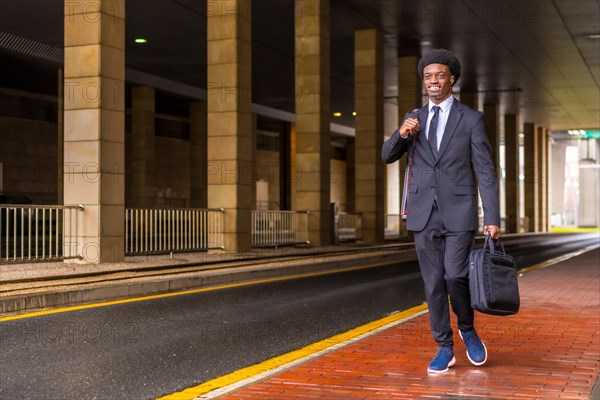 Horizontal photo with copy space of an african architect holding computer bag and drawings tube walking in the city