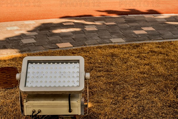 Outdoor LED light casting a shadow on the grass next to a paved path, in South Korea