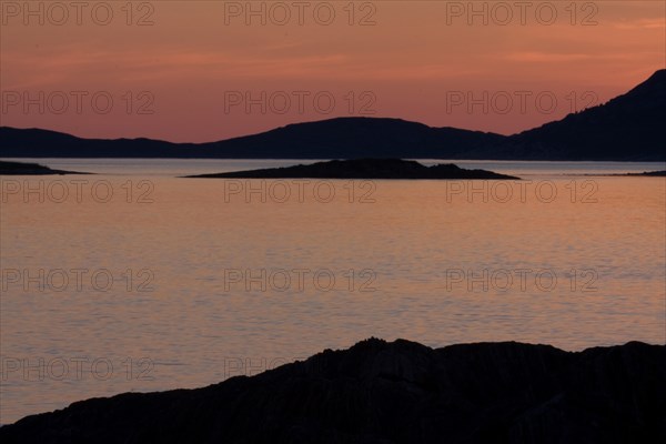 A calm sunset with orange and purple sky over the sea and mountain silhouettes Lofoten Norway