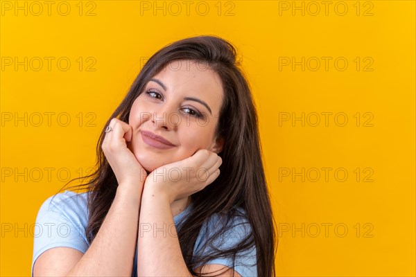Studio portrait with yellow background of a cute woman looking at camera hands on chin