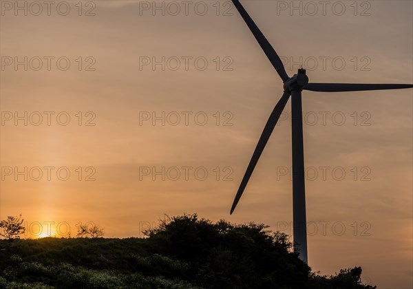 Wind turbine silhouette against cloudy sky as sun sets behind mountain top in South Korea