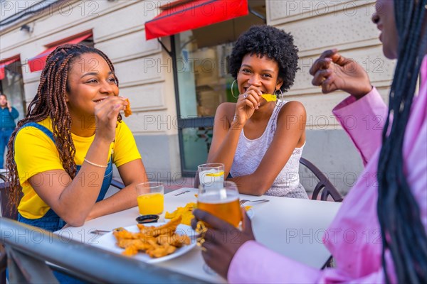 Three female young african friends eating fast food with beer in an outdoor restaurant