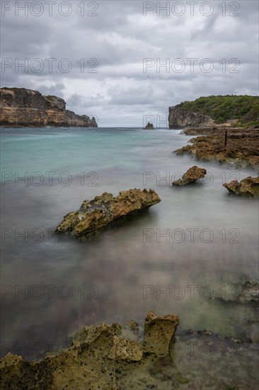 Rocky coast, long bay by the sea at sunset. Dangerous view of the Caribbean Sea. Tropical climate on a cloudy day in La Porte d'Enfer, Grande Terre, Guadeloupe, French Antilles, North America